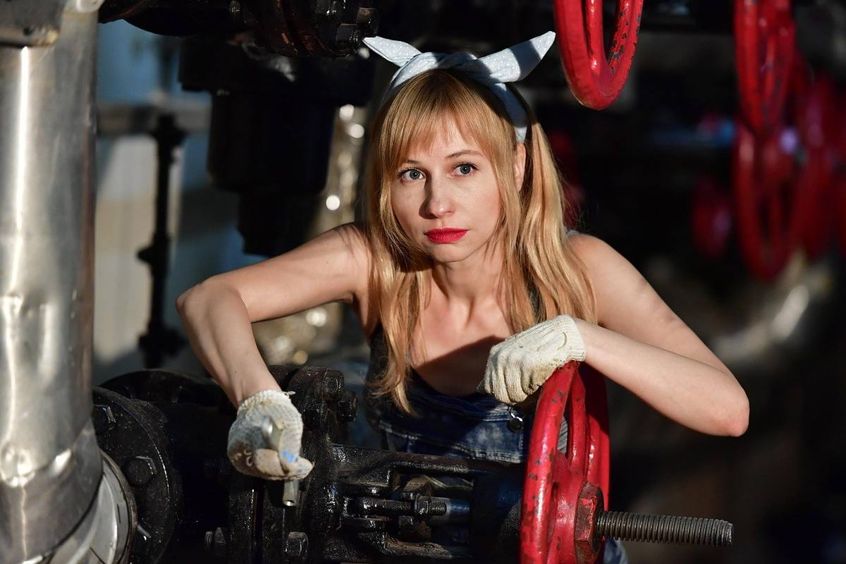 Femme en combinaison usagère manipulant une manivelle rouge dans un environnement industriel