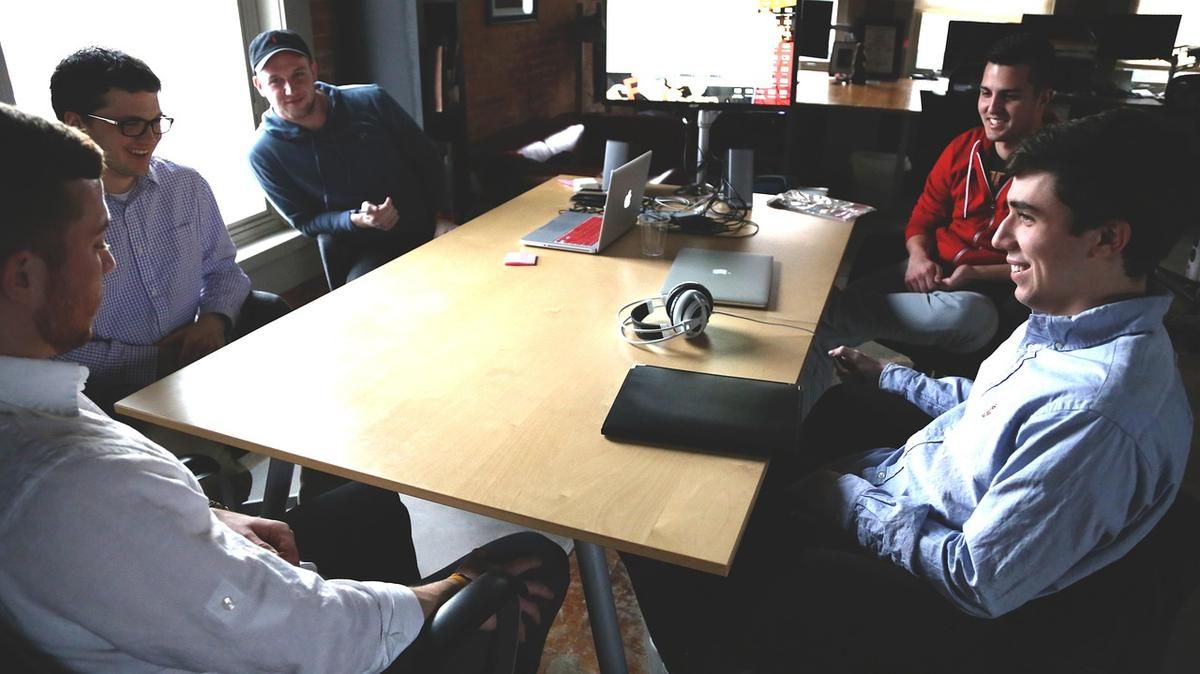 Six hommes assis autour d'une table de travail avec ordinateurs portables
